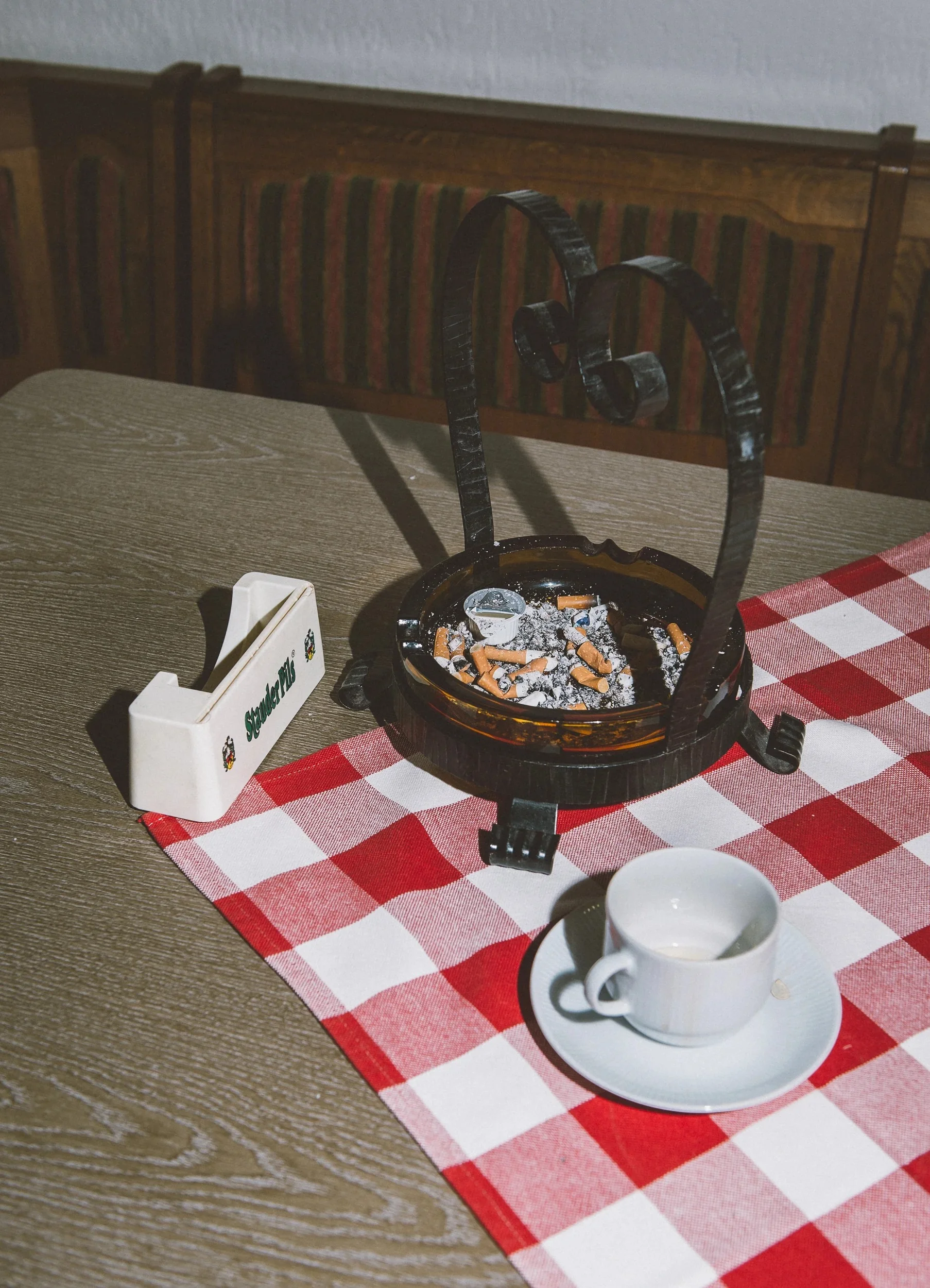 Still life including an ashtray and coffee cup on a red and white checkered tablecloth.